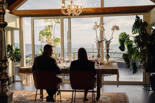 A couple at a candlelit table beside large windows