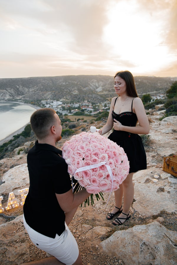 A man kneeling with pink roses during a seaside proposal