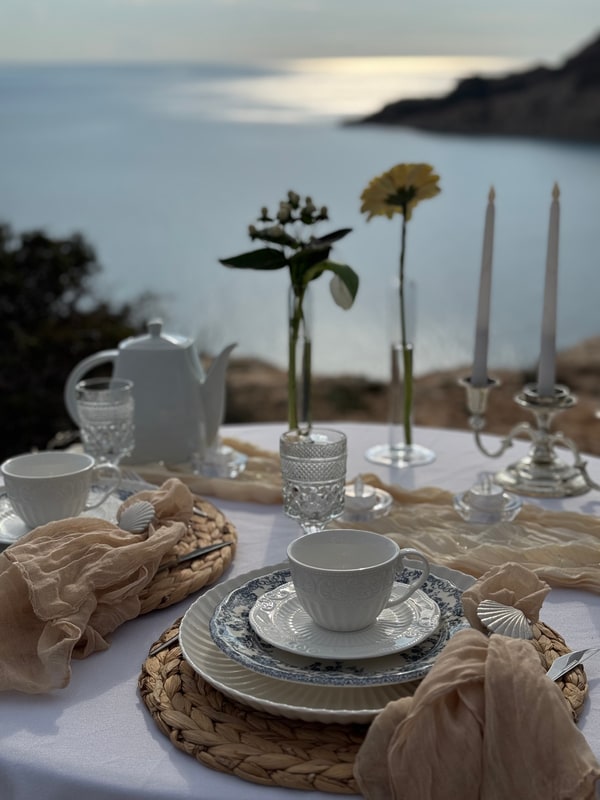A seaside picnic table with teacups, pale fabric and candles