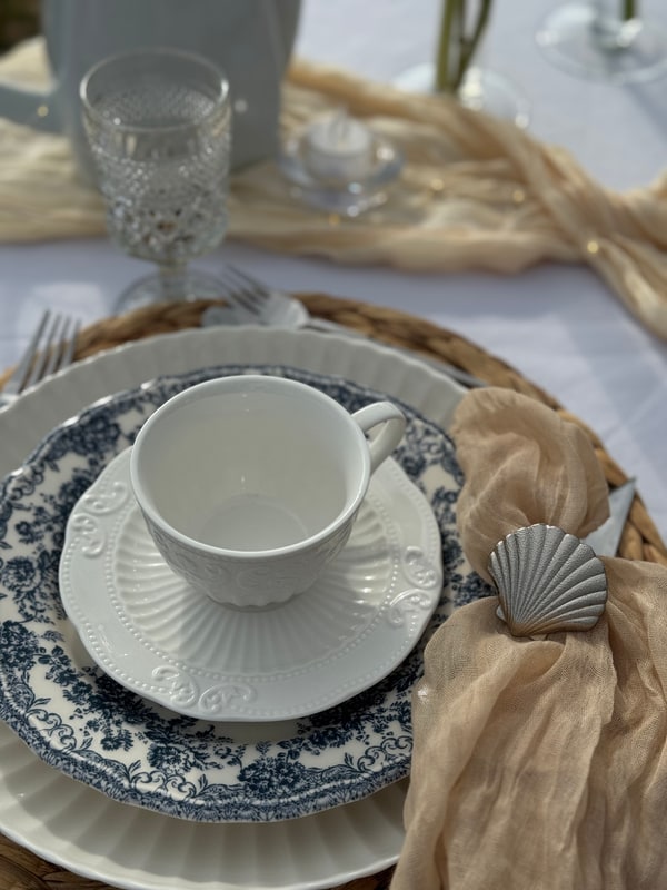 A seaside picnic table with teacups, pale fabric and candles