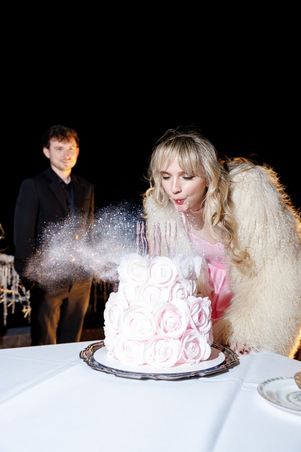A pink birthday cake and guests gathered on the terrace at night