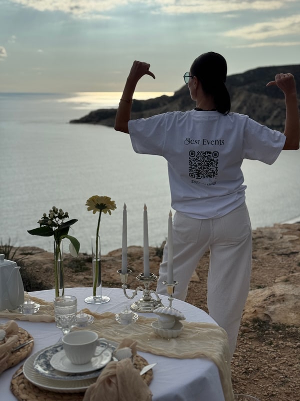 A woman standing beside the picnic table with the coast behind her