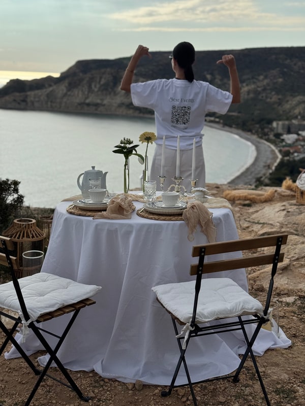 A woman standing beside the picnic table with the coast behind her