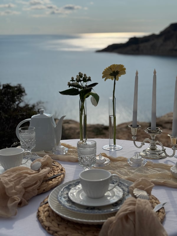 A seaside picnic table with teacups, pale fabric and candles