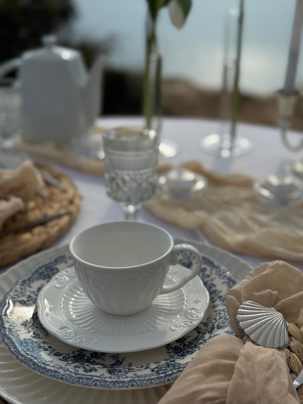 A seaside picnic table with teacups, pale fabric and candles