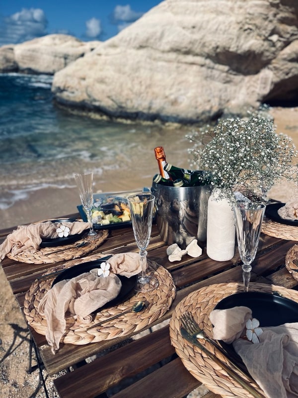 A picnic table with woven placemats and glassware beside the sea