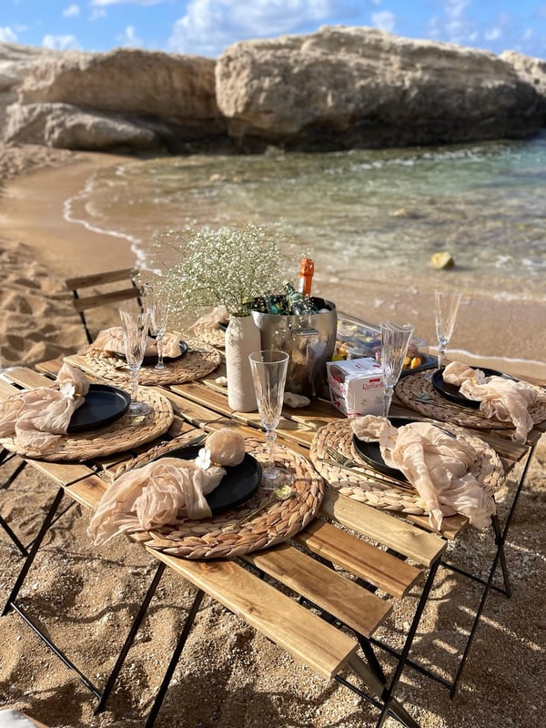 A picnic table with woven placemats and glassware beside the sea