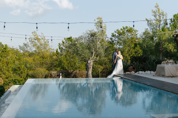 The couple beside a swimming pool beneath strings of lights