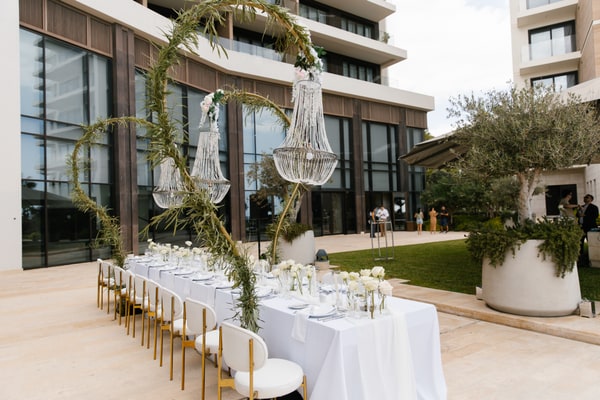 A long white reception table beneath suspended crystal chandeliers