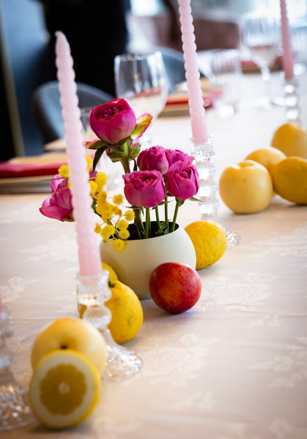 A long table with flowers, pink candles and lemons beneath chandeliers