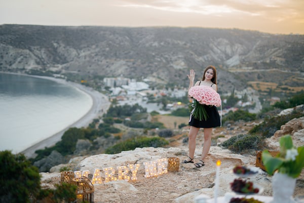 A woman holding pink roses with the bay behind her