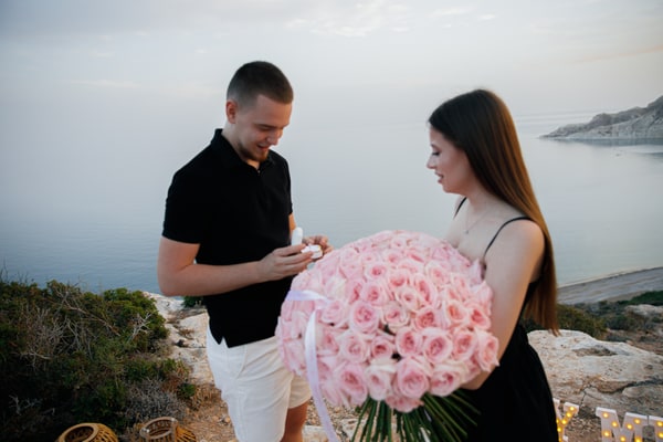 The couple looking at the engagement ring beside the roses